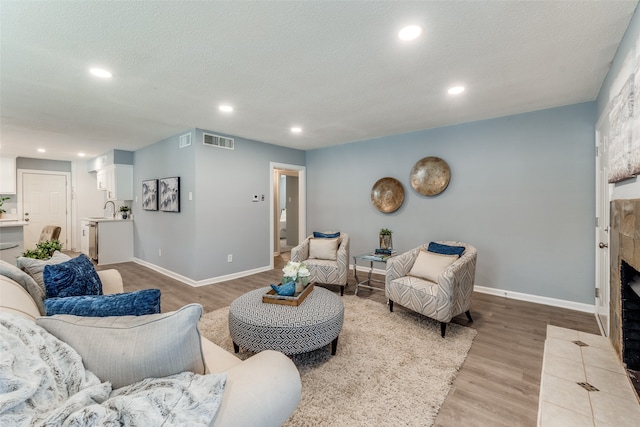 living room with a tile fireplace, sink, a textured ceiling, and light hardwood / wood-style floors