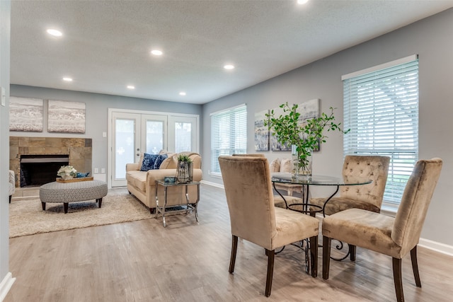 dining space featuring a tile fireplace, french doors, light hardwood / wood-style floors, and a textured ceiling