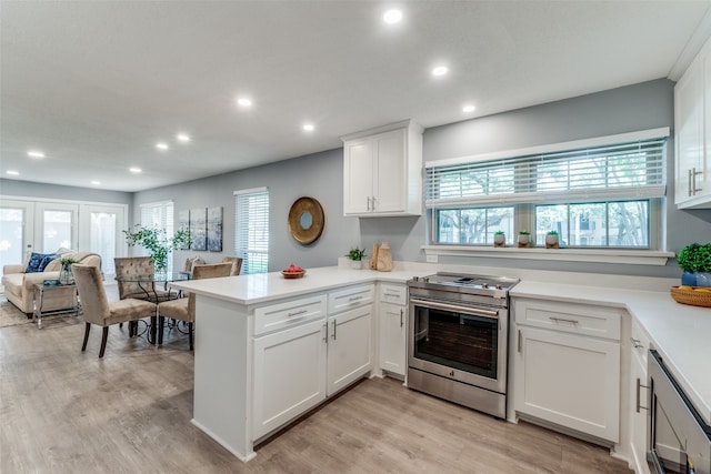 kitchen featuring plenty of natural light, stainless steel range oven, light wood-type flooring, and kitchen peninsula