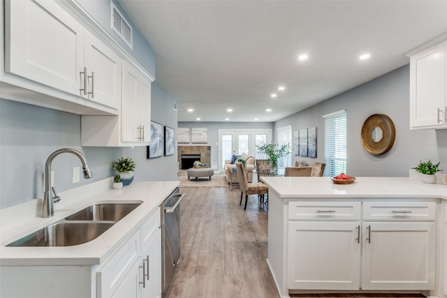 kitchen featuring light hardwood / wood-style flooring, white cabinets, stainless steel dishwasher, a fireplace, and sink