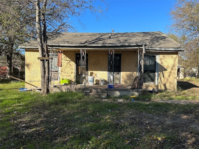 back of house with a shingled roof, covered porch, and brick siding