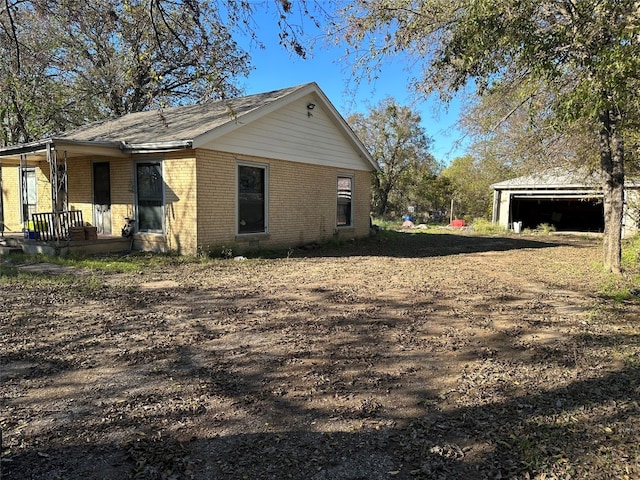 view of side of property with covered porch, brick siding, and an outdoor structure