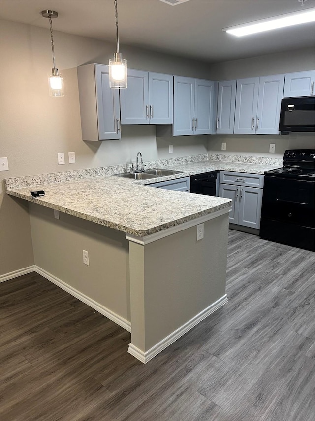 kitchen with a peninsula, a sink, black appliances, dark wood finished floors, and decorative light fixtures