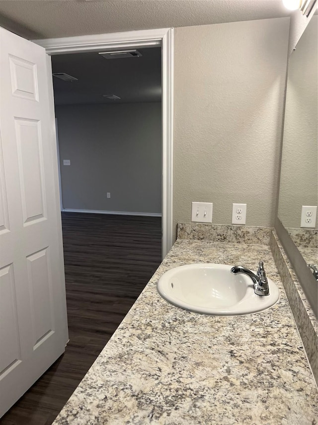 bathroom featuring visible vents, a textured wall, vanity, and wood finished floors