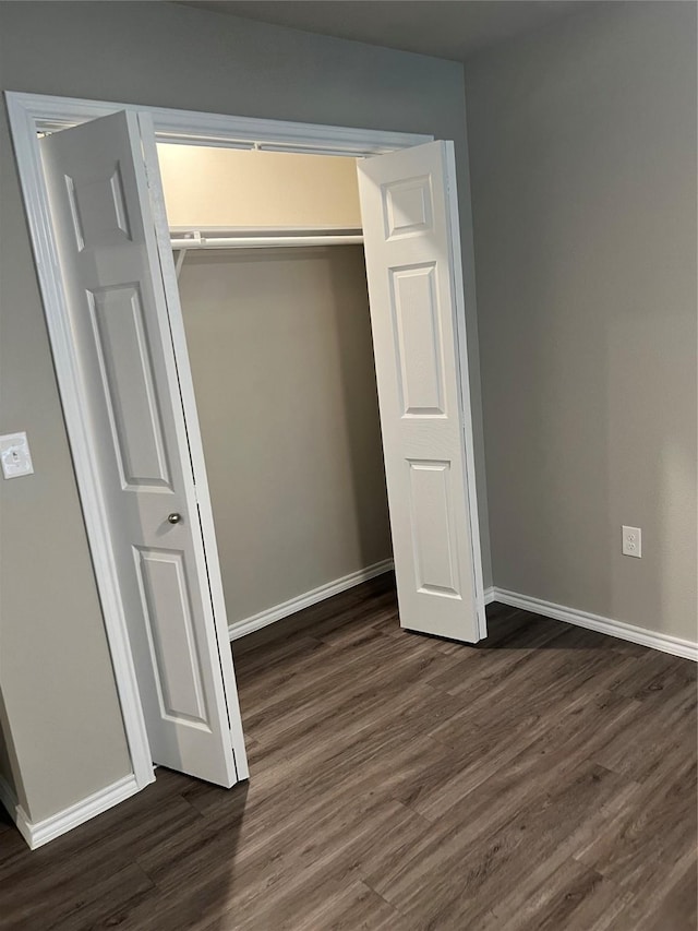 unfurnished bedroom featuring dark wood-style floors, baseboards, and a closet