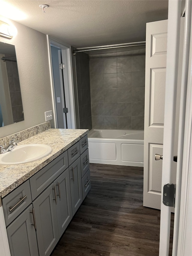 bathroom with a textured ceiling, vanity, hardwood / wood-style flooring, and tiled shower / bath combo