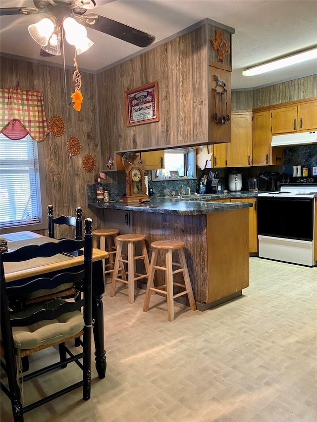 kitchen featuring kitchen peninsula, backsplash, white electric range oven, a breakfast bar area, and wood walls