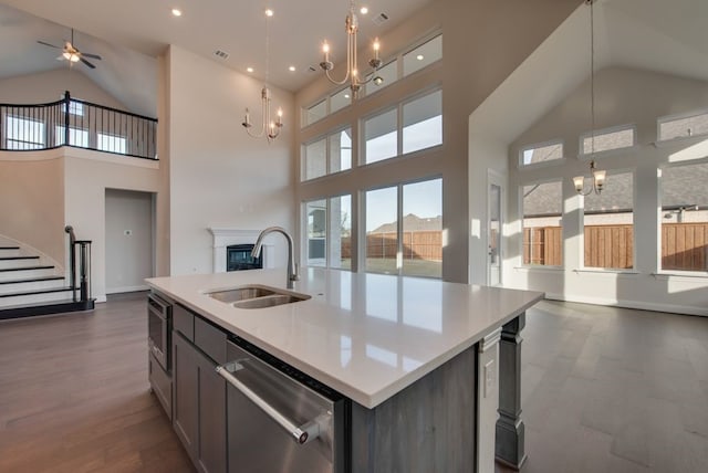 kitchen with a towering ceiling, stainless steel appliances, sink, pendant lighting, and an island with sink