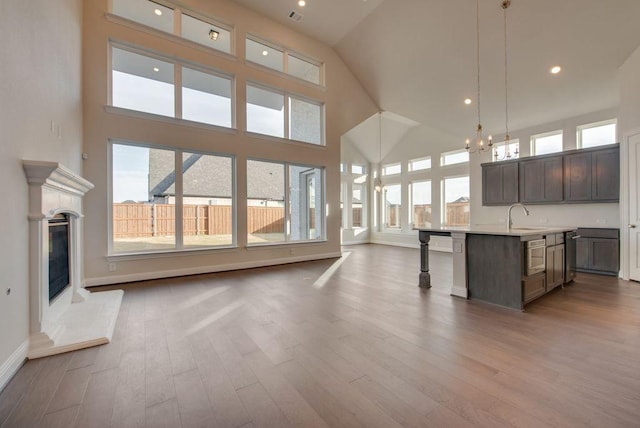 kitchen with a high ceiling, dark brown cabinetry, decorative light fixtures, hardwood / wood-style floors, and an island with sink