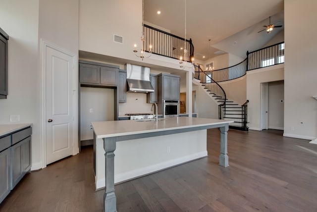 kitchen featuring a breakfast bar, a towering ceiling, wall chimney exhaust hood, and stainless steel oven