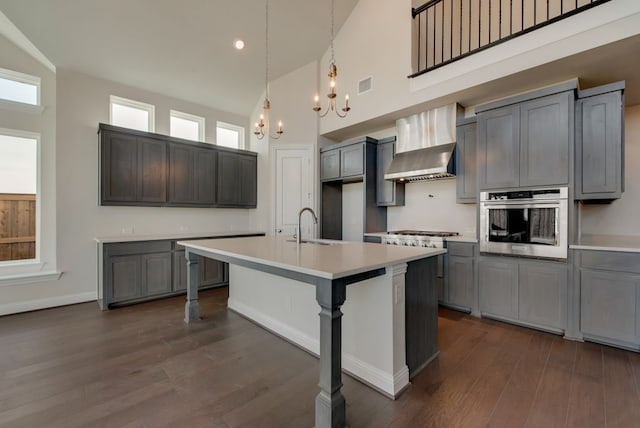 kitchen featuring a center island with sink, wall chimney exhaust hood, stainless steel oven, and high vaulted ceiling