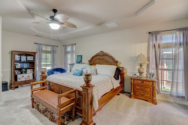 carpeted bedroom with ceiling fan and a tray ceiling