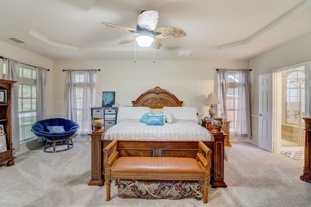 carpeted bedroom featuring ceiling fan, ensuite bathroom, and a tray ceiling