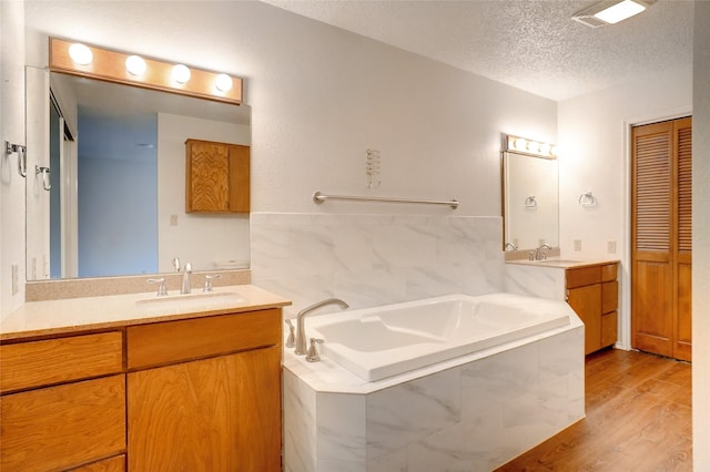 bathroom featuring vanity, wood-type flooring, a textured ceiling, and tiled tub