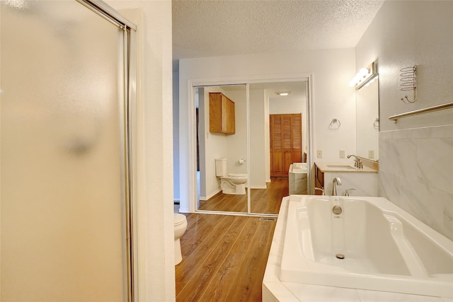 full bathroom featuring hardwood / wood-style floors, vanity, plus walk in shower, toilet, and a textured ceiling