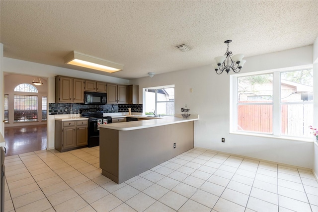 kitchen featuring backsplash, black appliances, light tile patterned floors, kitchen peninsula, and a chandelier