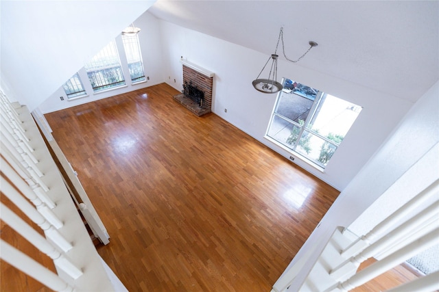 unfurnished living room featuring a fireplace, high vaulted ceiling, a notable chandelier, and hardwood / wood-style flooring