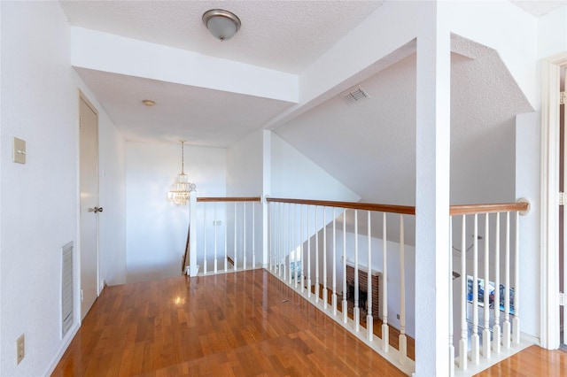 hall with wood-type flooring, a textured ceiling, and a notable chandelier