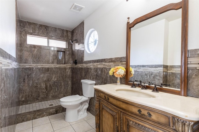 bathroom with tile patterned flooring, tiled shower, toilet, vanity, and tile walls