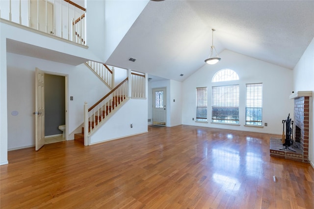 unfurnished living room featuring wood-type flooring, a textured ceiling, high vaulted ceiling, and a brick fireplace