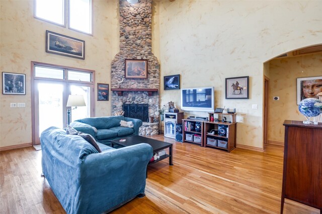 living room featuring a stone fireplace, hardwood / wood-style floors, a towering ceiling, and a healthy amount of sunlight