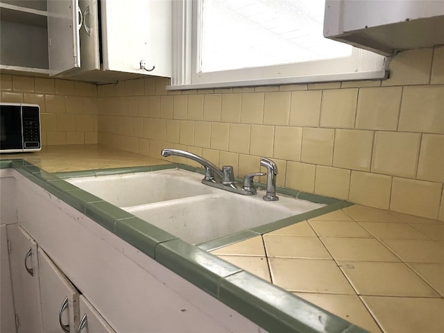 kitchen featuring white cabinets, tile countertops, tasteful backsplash, and sink