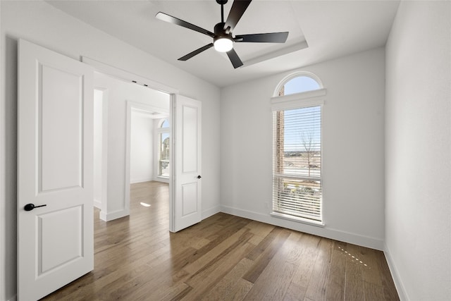 unfurnished room with a raised ceiling, ceiling fan, and dark hardwood / wood-style flooring