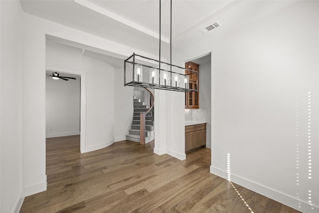 unfurnished dining area featuring dark hardwood / wood-style flooring and ceiling fan with notable chandelier