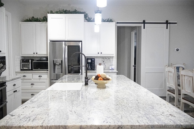 kitchen featuring a barn door, tasteful backsplash, white cabinetry, and an island with sink