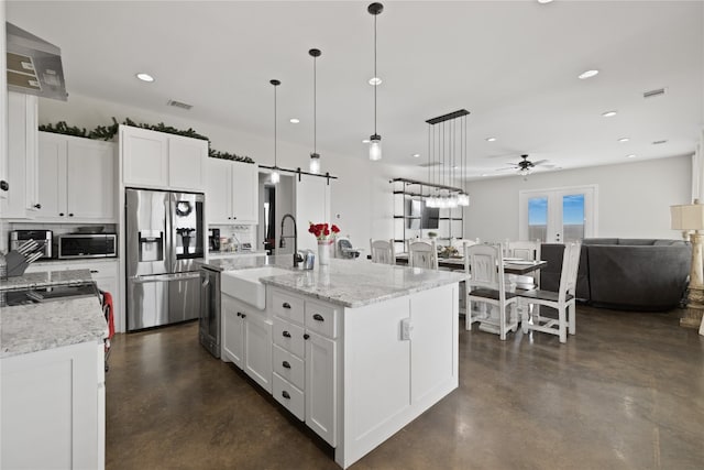 kitchen with appliances with stainless steel finishes, sink, white cabinets, hanging light fixtures, and an island with sink