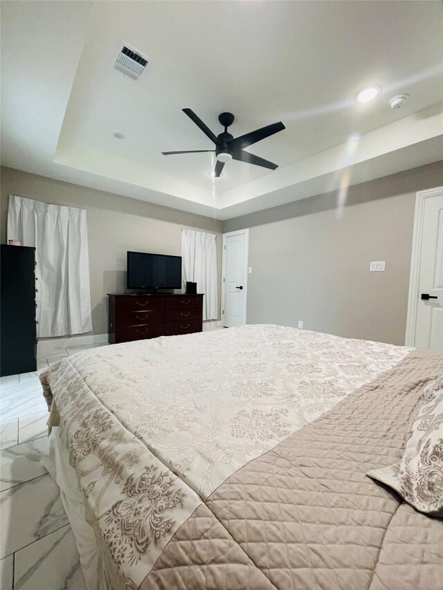 tiled bedroom with ceiling fan and a raised ceiling