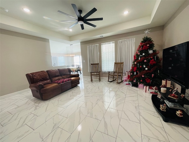 living room featuring light tile patterned flooring, ceiling fan, and a tray ceiling