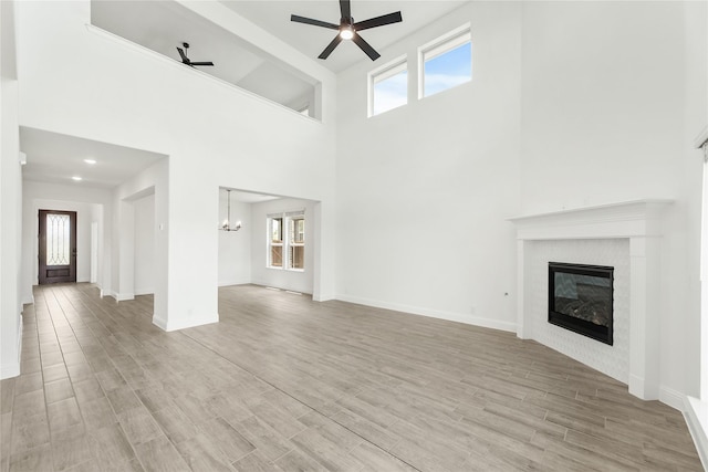 unfurnished living room featuring ceiling fan with notable chandelier, a high ceiling, and light wood-type flooring