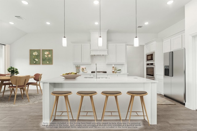 kitchen featuring a center island with sink, stainless steel appliances, hanging light fixtures, and white cabinets