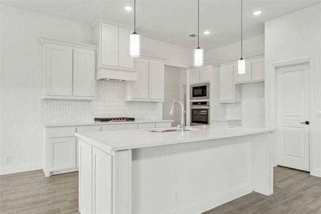 kitchen with sink, stainless steel oven, hanging light fixtures, a center island with sink, and white cabinets