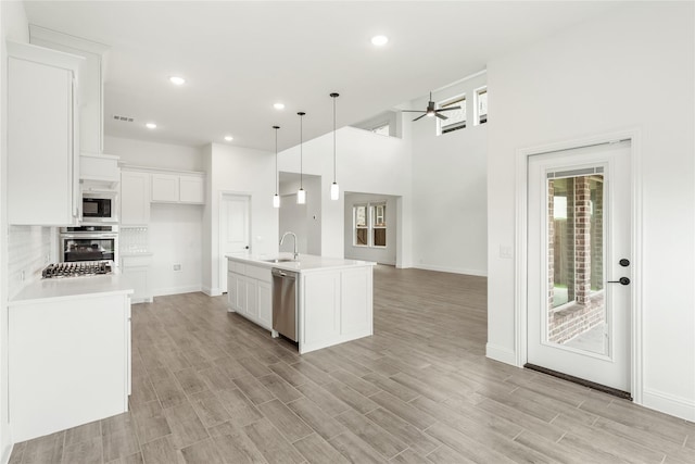 kitchen with sink, white cabinetry, stainless steel appliances, a center island with sink, and decorative light fixtures