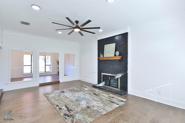 living room with crown molding, ceiling fan, wood-type flooring, and a brick fireplace