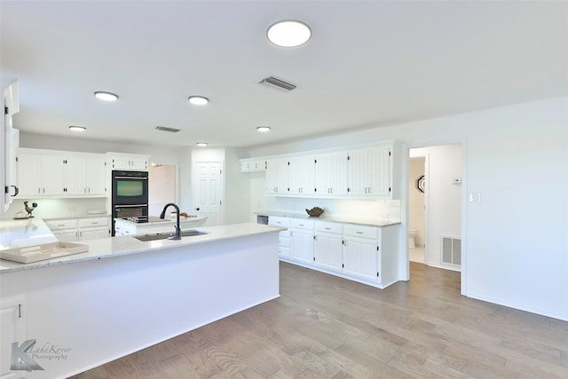 kitchen with sink, white cabinetry, light stone counters, light hardwood / wood-style flooring, and black double oven