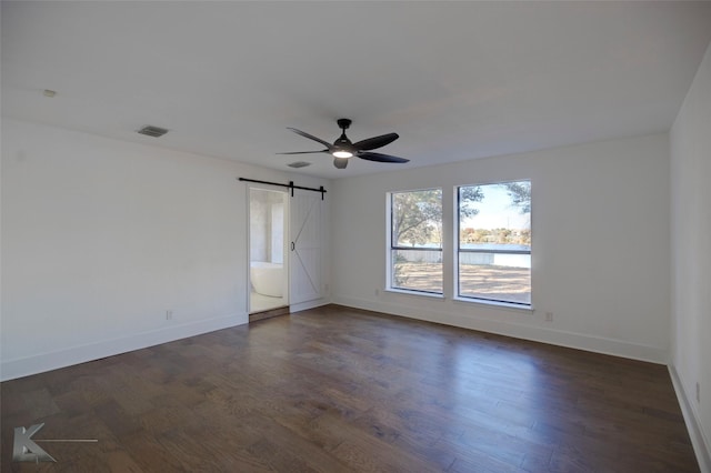 spare room featuring ceiling fan, a barn door, and dark hardwood / wood-style flooring