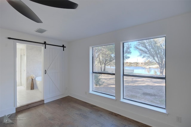 unfurnished room with a barn door, wood-type flooring, a water view, and plenty of natural light