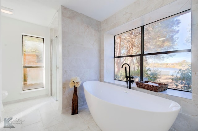 bathroom featuring a washtub, a healthy amount of sunlight, and tile walls