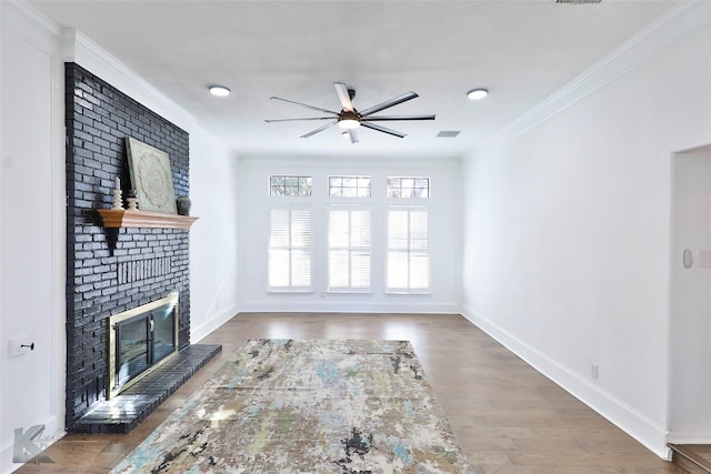 unfurnished living room with crown molding, a brick fireplace, dark wood-type flooring, and ceiling fan