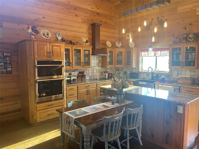 kitchen featuring hanging light fixtures, custom exhaust hood, decorative backsplash, wooden walls, and appliances with stainless steel finishes