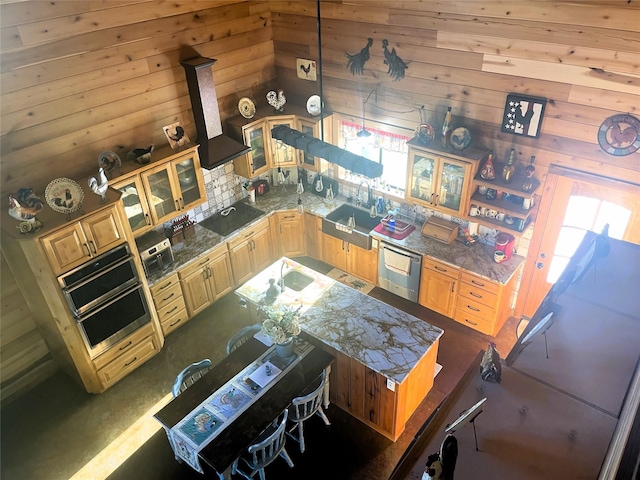 kitchen featuring glass insert cabinets, appliances with stainless steel finishes, light brown cabinetry, a sink, and wooden walls