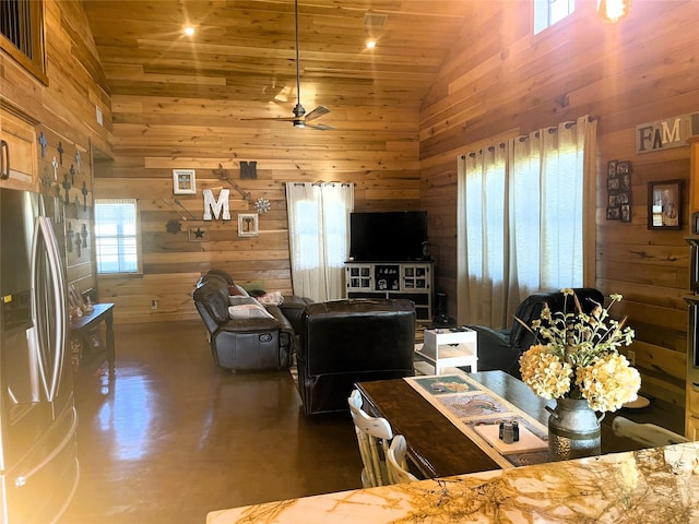 living area with wooden walls, high vaulted ceiling, finished concrete flooring, and a ceiling fan
