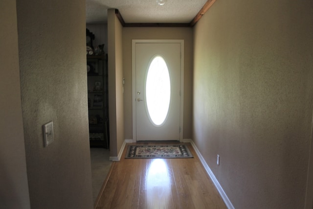 doorway featuring hardwood / wood-style flooring, a textured ceiling, and ornamental molding