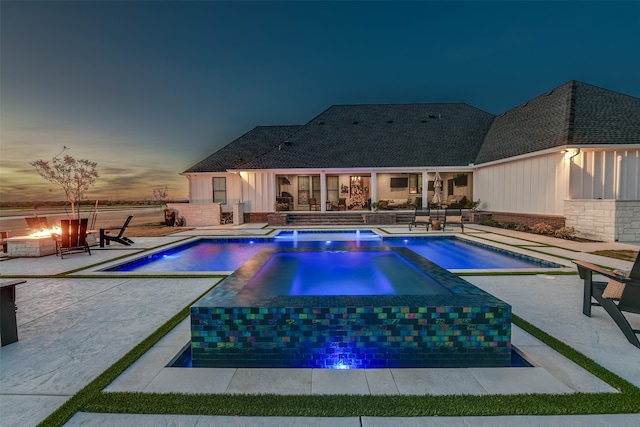 pool at dusk featuring a fire pit, an in ground hot tub, and a patio