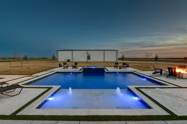 pool at dusk with pool water feature, a patio area, and an outdoor fire pit