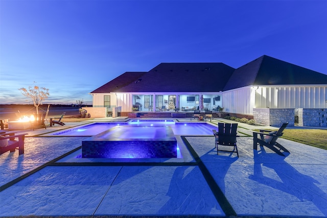 pool at dusk with a patio and an in ground hot tub