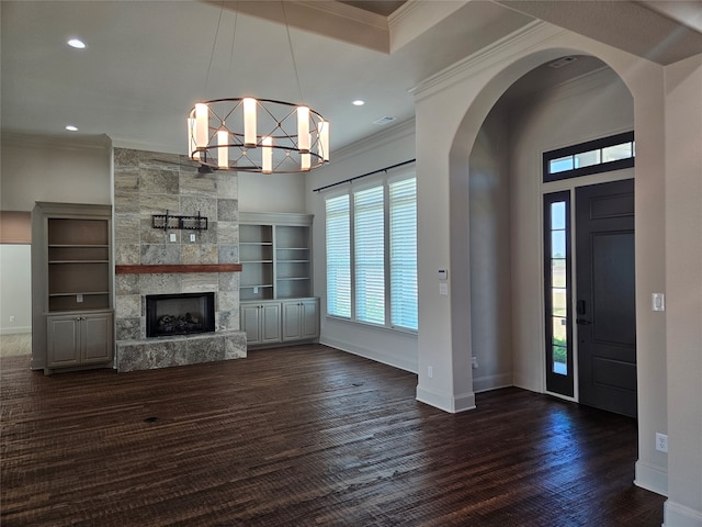 entryway featuring a notable chandelier, ornamental molding, dark wood-type flooring, and a stone fireplace